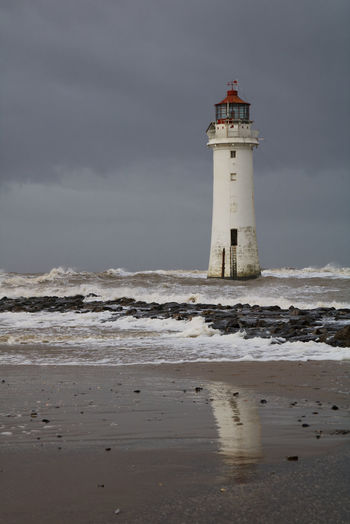 Lighthouse on beach by sea against sky