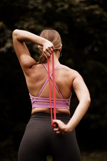 Rear view of woman standing against blurred background with a stretching band