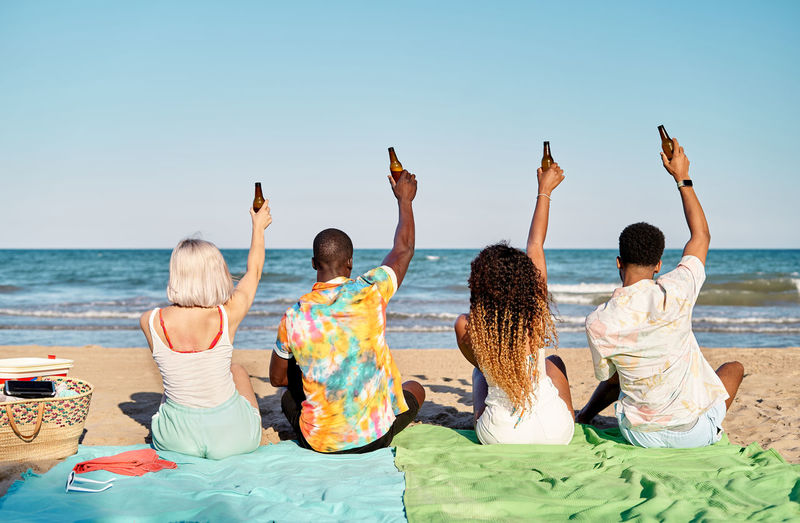 Rear view of woman sitting on beach against clear sky