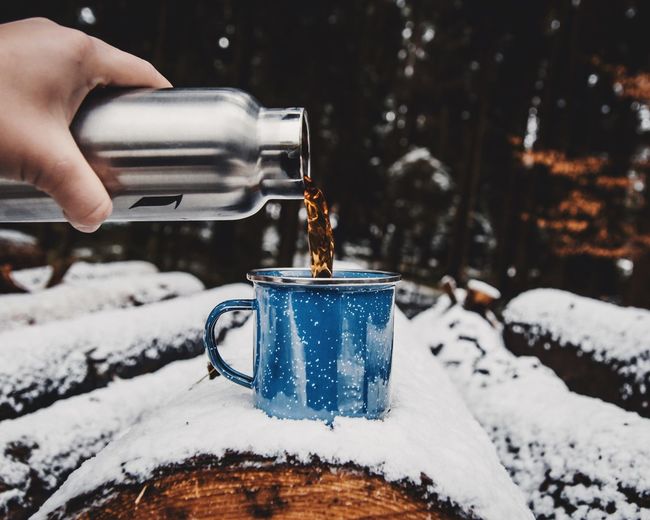 Cropped hand pouring tea in cup on snow covered log