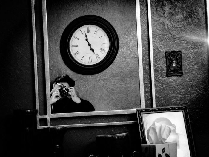 Reflection of woman photographing through camera against wall clock at home