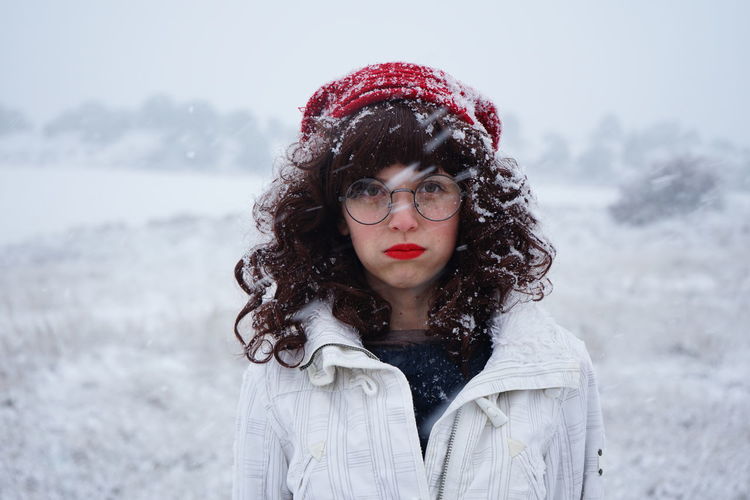 Portrait of young woman standing on field during snowfall