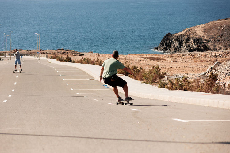 Two men playing figure skating on a rural road in the sun on a bright day,play surf skate near coast
