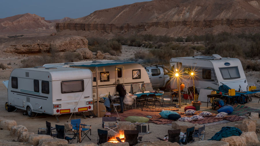 Vehicle trailers and camping chairs in desert during sunset