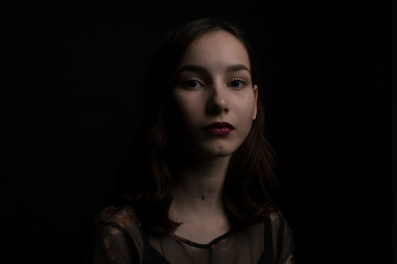 Close-up portrait of beautiful young woman over black background