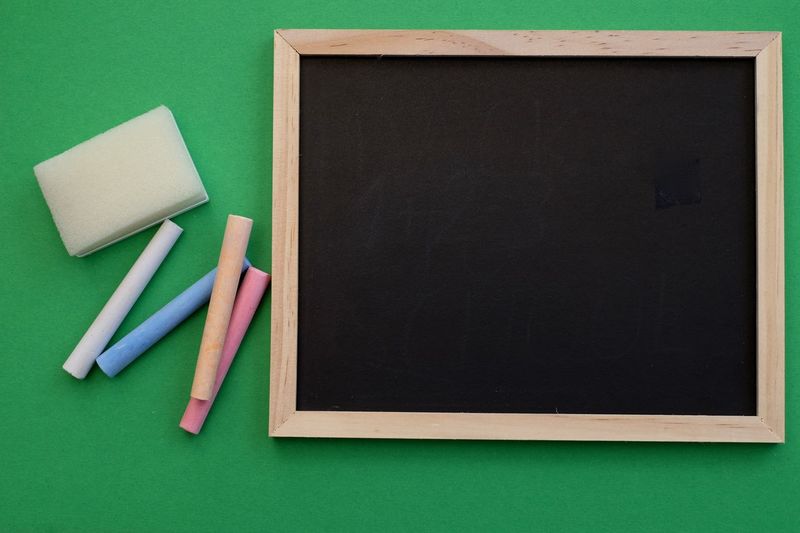 Directly above shot of blank chalkboard by chalks over green background