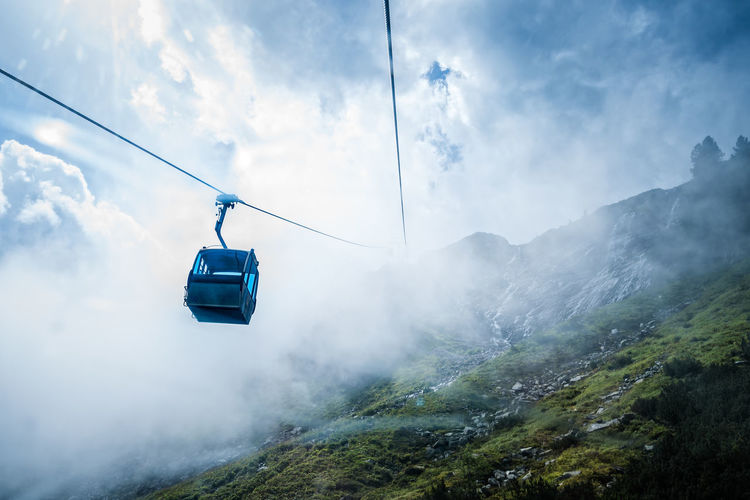 Low angle view of overhead cable car at mountains against cloudy sky