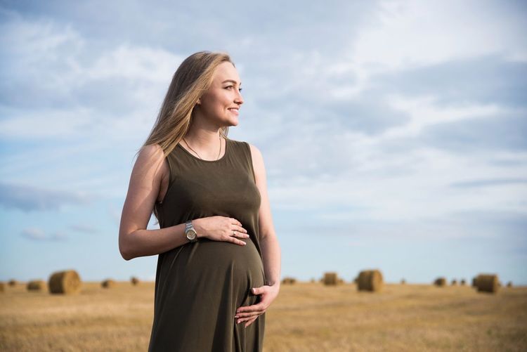 Smiling pregnant woman standing on field against sky