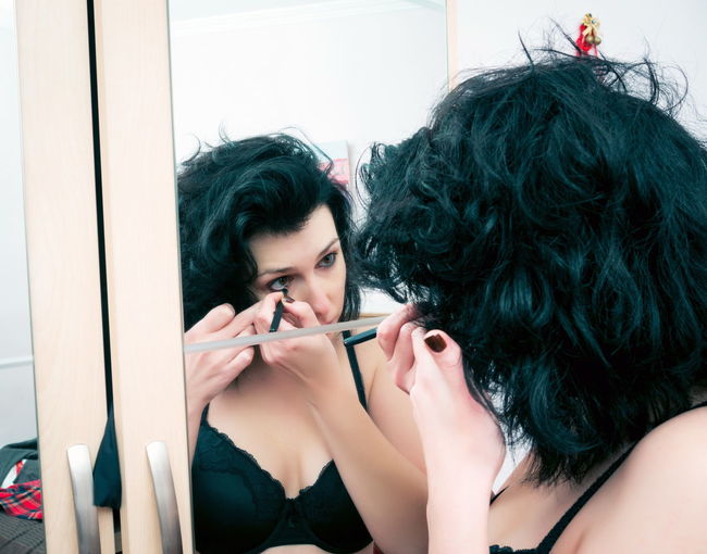 Close-up of beautiful woman applying make-up reflecting on mirror at home