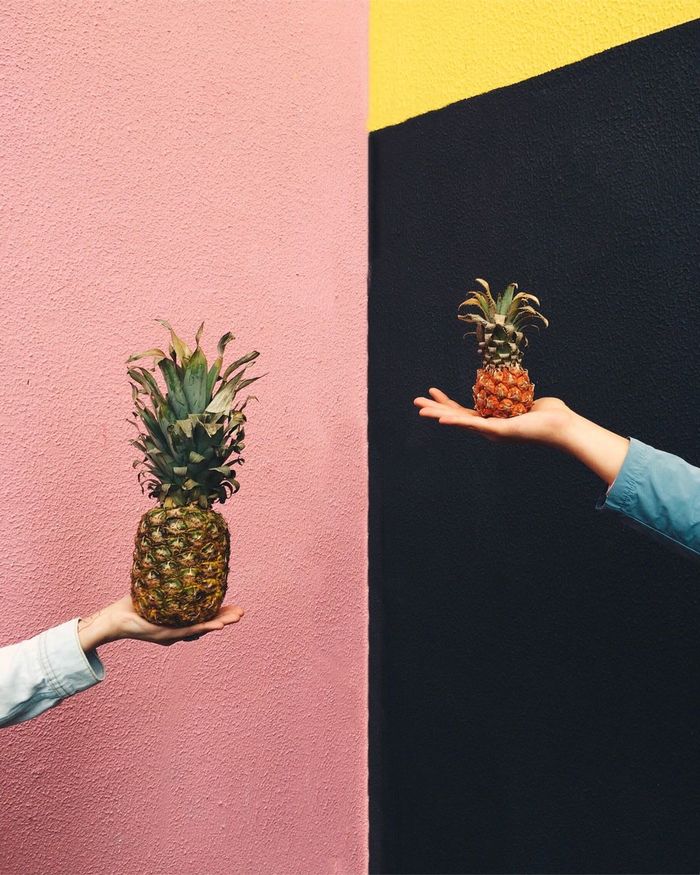 Two people holding pineapples against multi colored wall