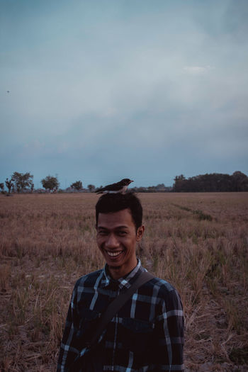 Bird perching smiling young man standing on field