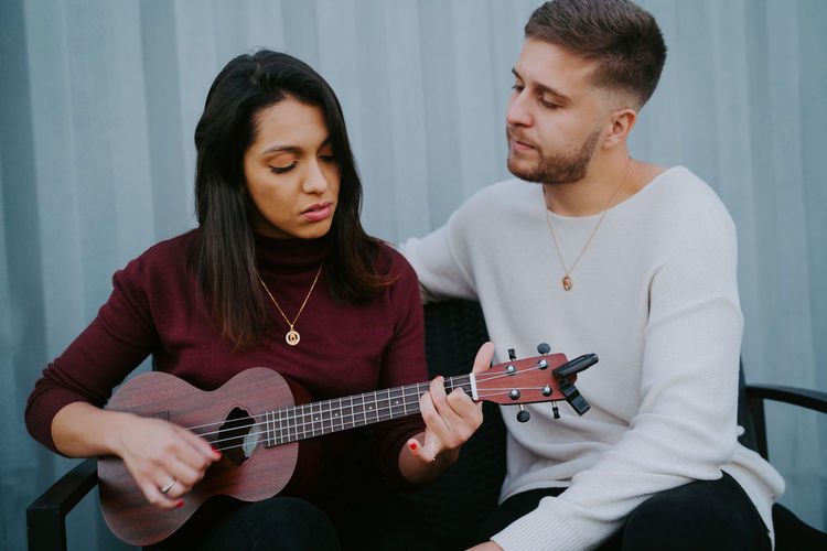 Tranquil couple sitting on backyard of container house and playing ukulele while enjoying music in evening