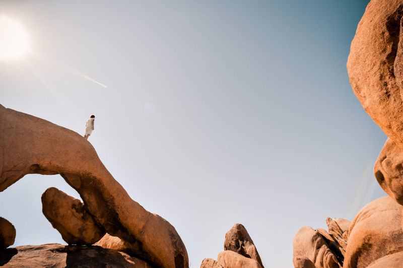Low angle view of woman standing on rock formation against sky during sunny day