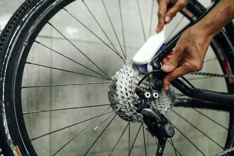 Unrecognizable crop male mechanic cleaning gear cassette of bicycle wheel with brush in workshop