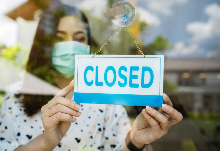 Close-up of woman wearing mas holding closed sign at cafe