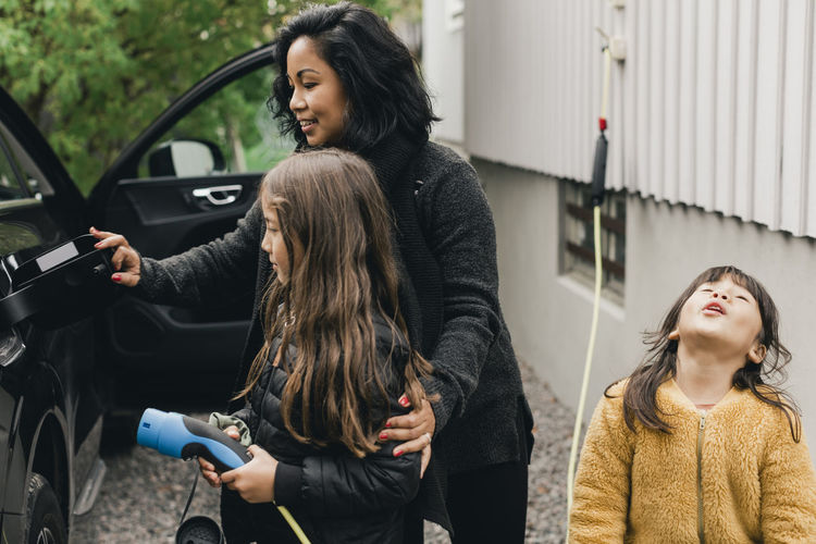 Woman teaching daughter to charge electric car at charging station