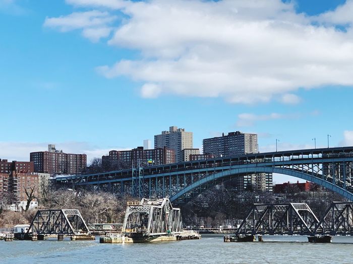 Bridge over river by buildings in city against sky