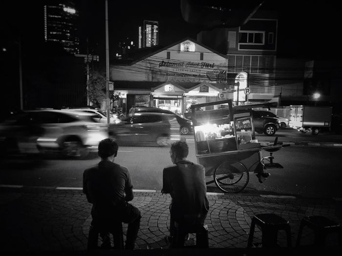 Rear view of friends sitting footpath at night