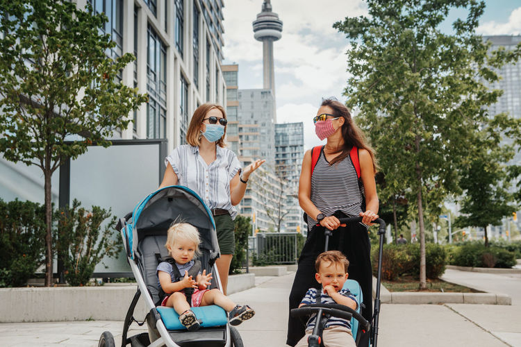 Two mothers walking with kids in strollers. social distance covid-19 coronavirus. new normal