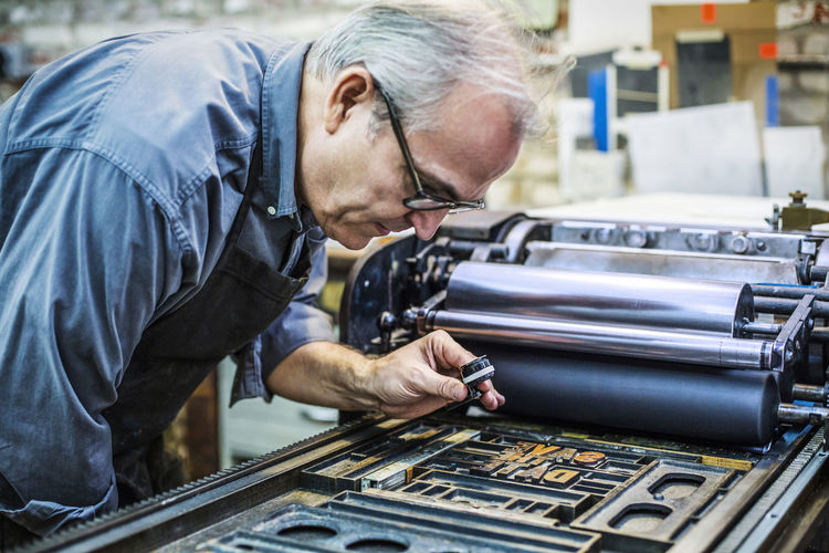 Side view of senior man examining letterpress through magnifying glass at workshop
