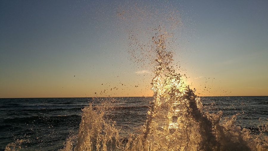 Wave splashing in sea against sky during sunset