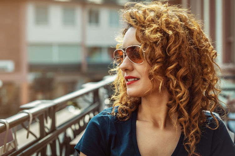 Young moroccan woman, with curly brown hair, sitting in an outdoor café in mainz, wearing sunglasses