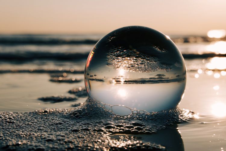 Close-up of crystal ball on beach against sky during sunset