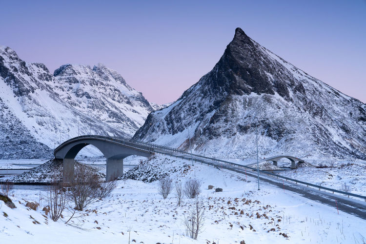 Bridge by snow covered mountains against clear sky