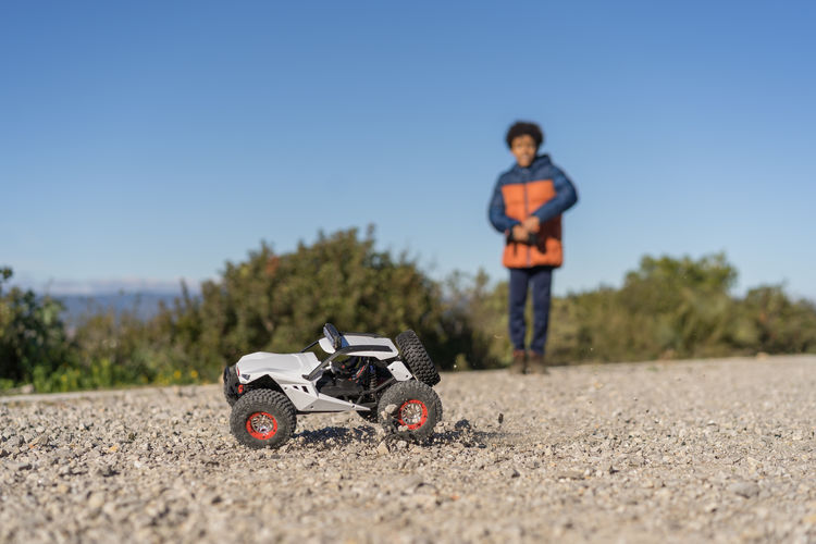 Cute afro kid with curly hair operating radio controlled car in the park. car out of focus