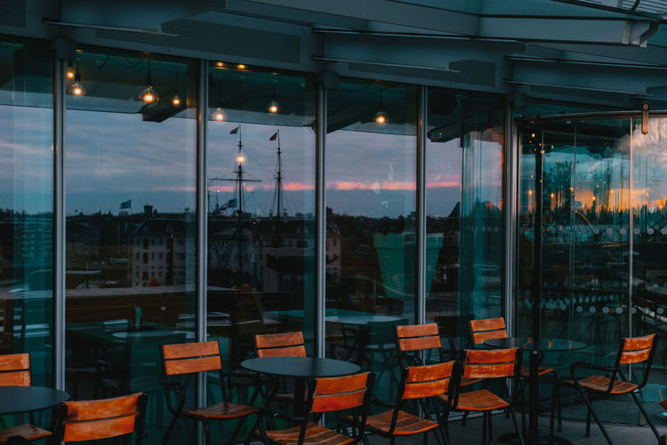 Empty chairs and tables in restaurant against sky at sunset