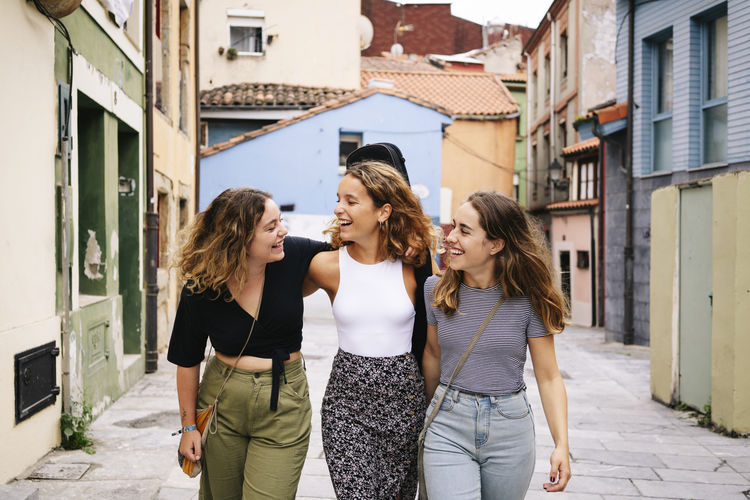 Meeting of young curly stylish women bonding and talking in city street