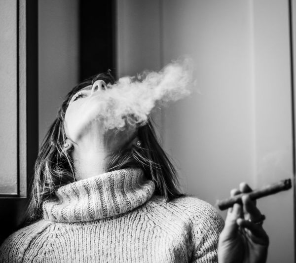 Close-up of woman smoking cigar against wall