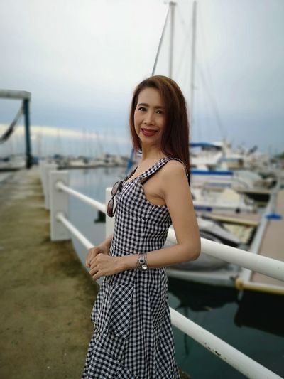 Portrait of smiling woman standing by railing at harbor