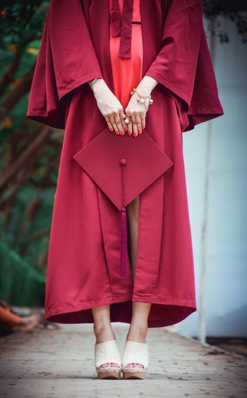 Low section of woman wearing graduation gown holding mortarboard
