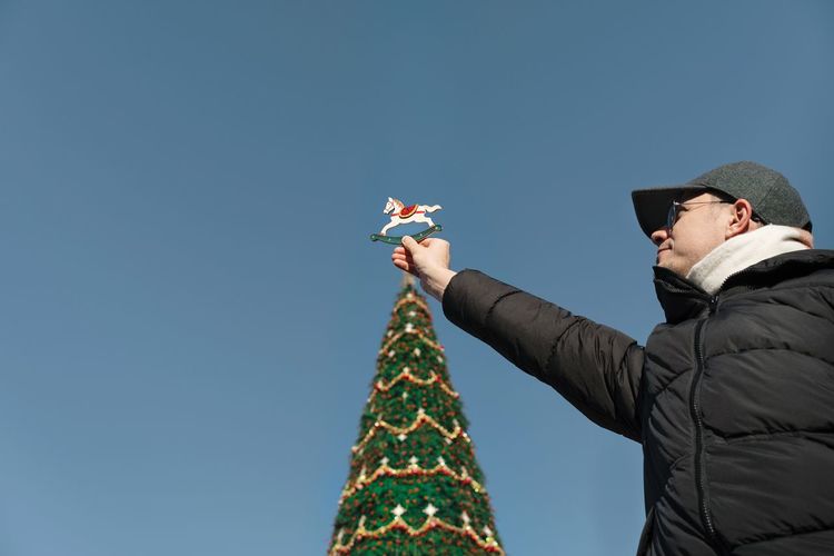 Low angle view of man holding tree topper against clear blue sky