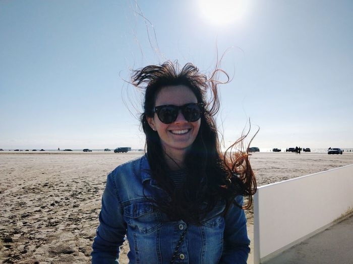 Portrait of smiling young woman on beach during sunny windy day