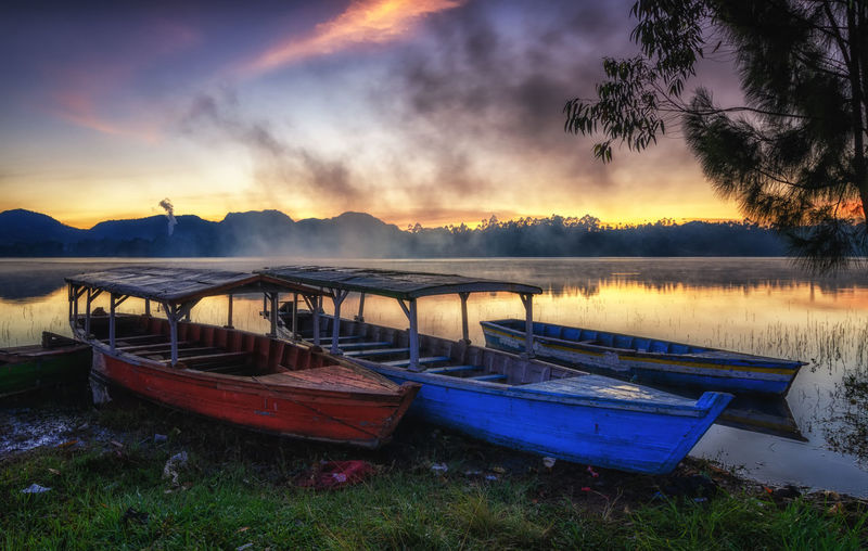 Boats moored on shore against sky during sunset