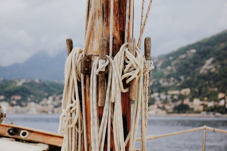 Close-up of rope tied on wooden post in sea against sky