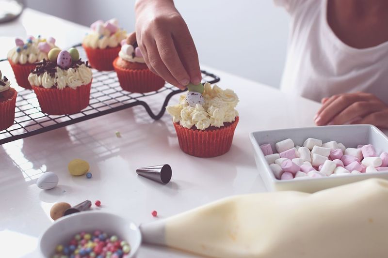 Midsection of person garnishing cupcakes on table at home