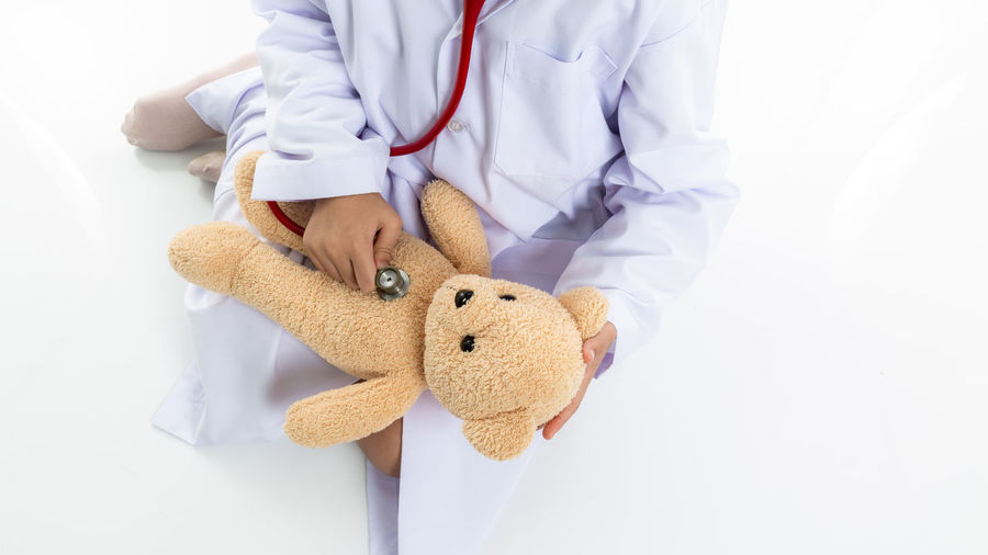 Midsection of doctor holding stuffed toy against white background