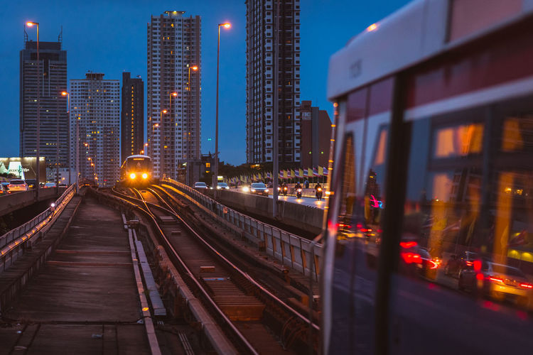 Illuminated railroad tracks amidst buildings in city at night