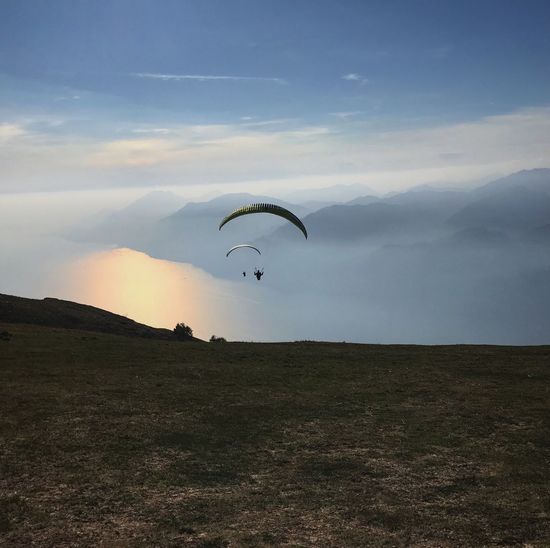 Silhouette people paragliding against cloudy sky during sunset