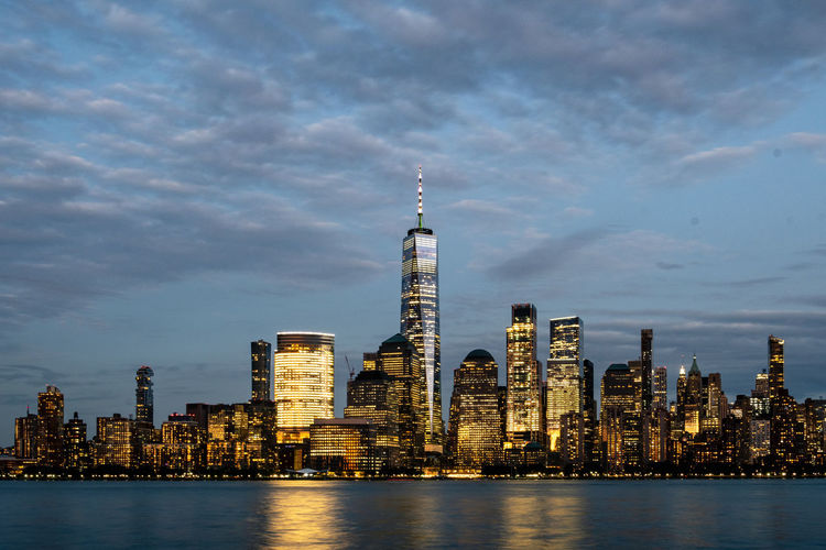 Illuminated buildings in city against cloudy sky