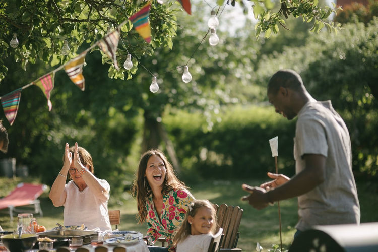 Cheerful multi-generation family with lunch at table in backyard during garden party