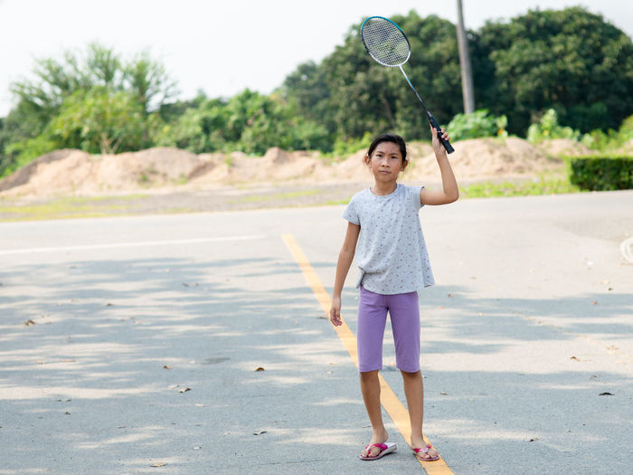 Full length of girl holding badminton racket while standing on road