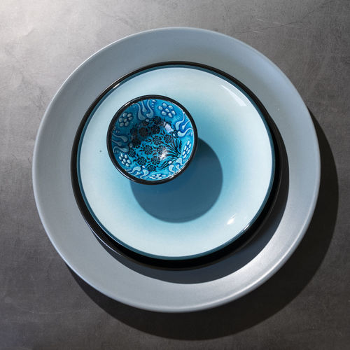 Tableware, different plates in grey blue colors on dark table with geometrical shapes shadows