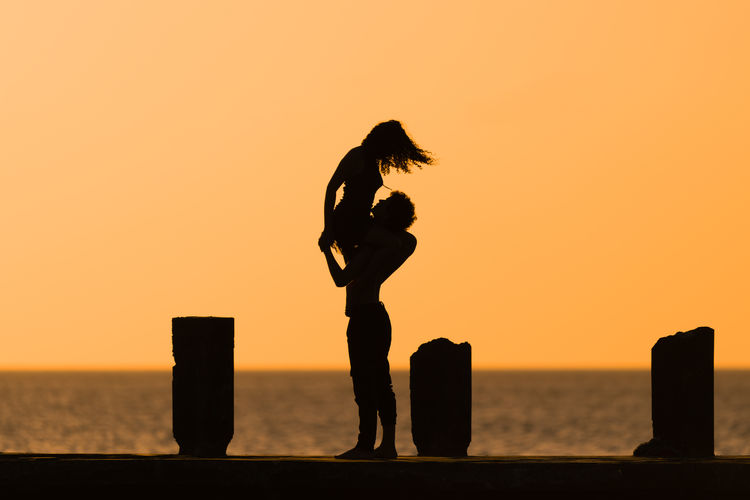 Silhouette dancers performing on beach against sky during sunset
