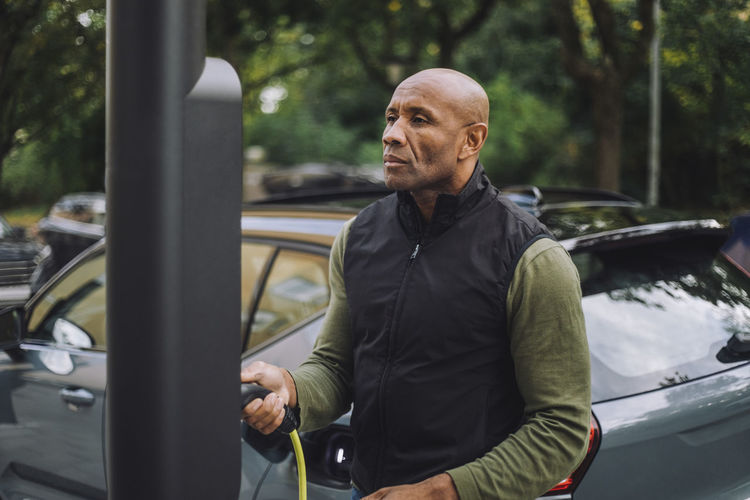 Bald mature man holding charging cable at car station