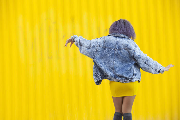 Rear view of woman dancing against yellow wall