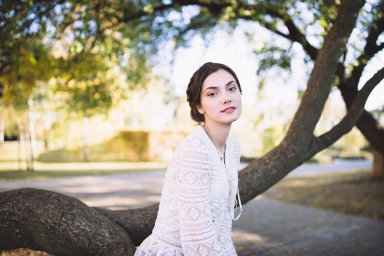 Beautiful brunette with braids around head in a vintage white lace long sleeve blouse in park
